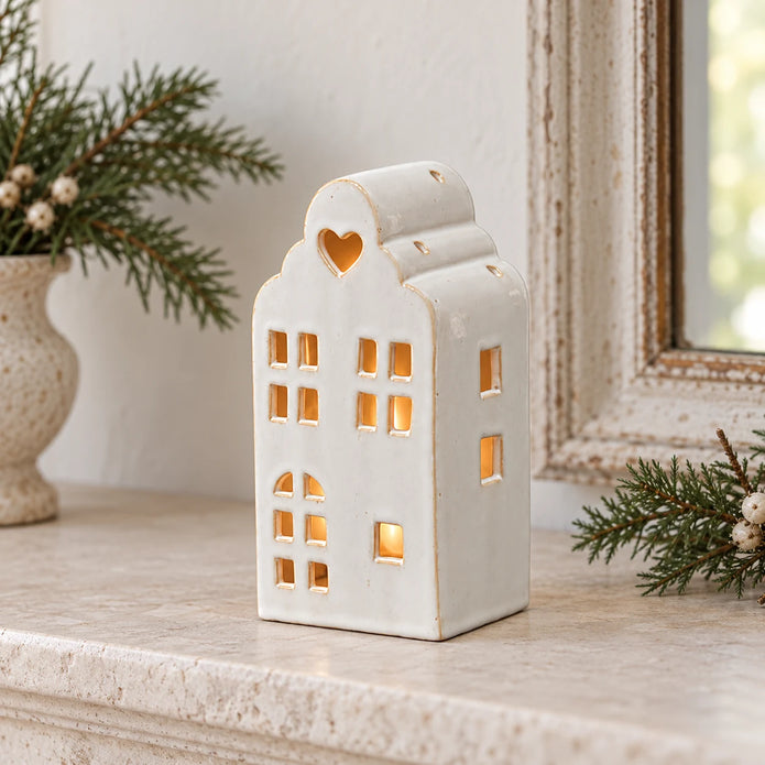 White ceramic house tealight holder glowing on a stone Christmas mantel