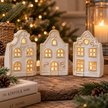 Three assorted white ceramic Dutch house tealight holders glowing on a rustic Christmas mantel display