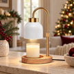 White enamel-effect candle warmer lamp with gold arm and wooden base on a Christmas console