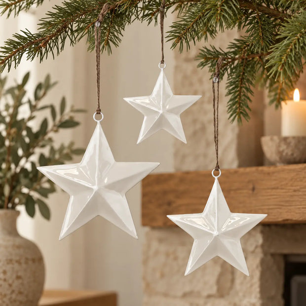 Three sizes of white enamel hanging star decorations on evergreen branches