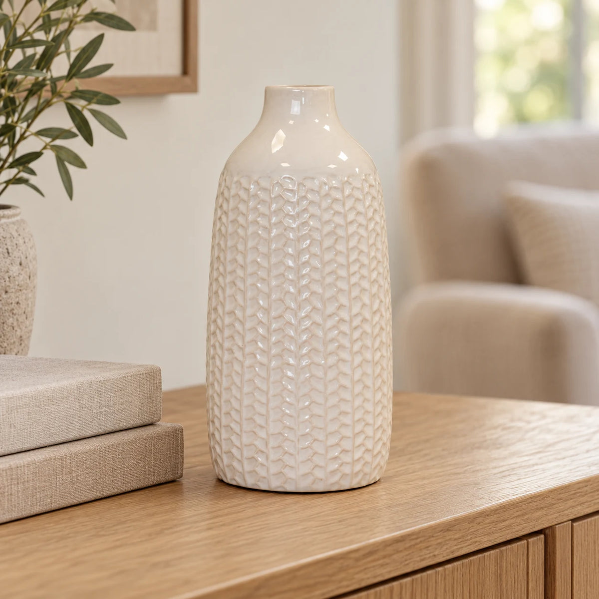 White leaf-patterned vase displayed empty beside neutral books in a bright living room