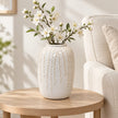 Medium warm white ceramic leaf vase styled with white blossom on a pale oak side table beside a cream linen armchair.