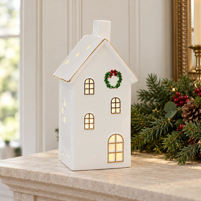 Large white LED Christmas house on a limestone mantel with greenery