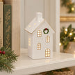 Medium white LED Christmas house styled beside books on a cream shelf