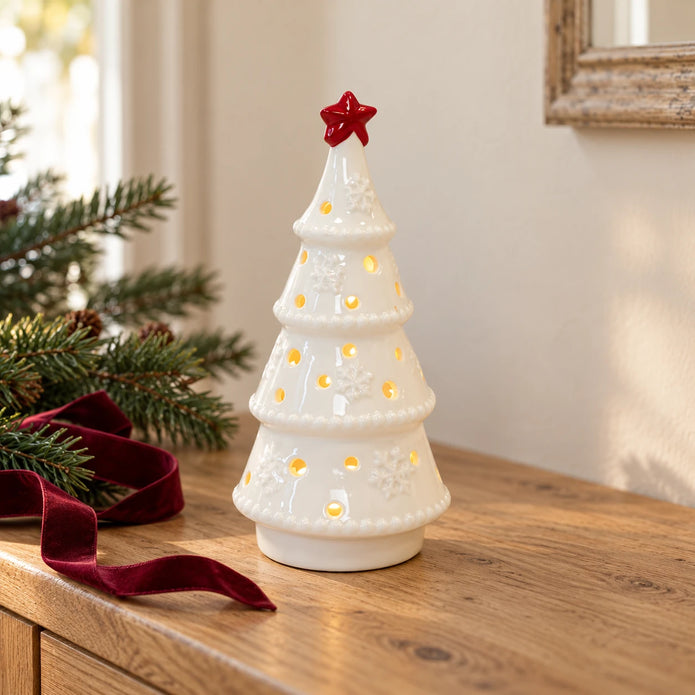 White ceramic LED tree with red star glowing on an oak console with fir and burgundy ribbon.