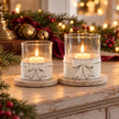 White bow hurricane tealight holders glowing in a Christmas console display with burgundy ribbon and bells