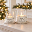 White metal bow hurricane tealight holders with candlelight and Christmas mantel greenery
