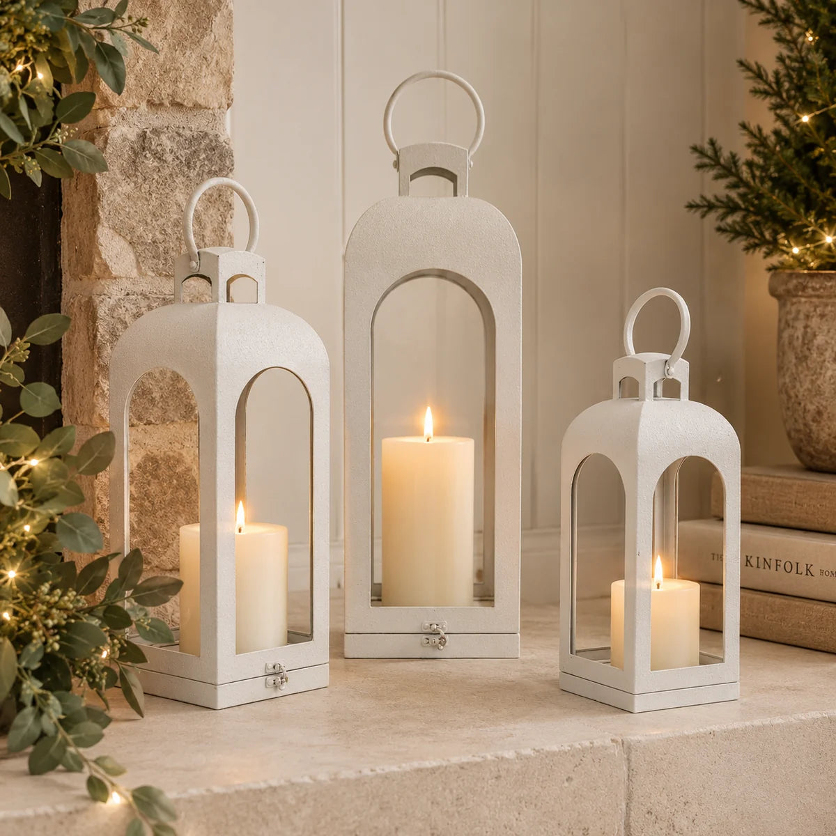 Three sizes of white open-sided metal lanterns with LED candles styled together on stone hearth