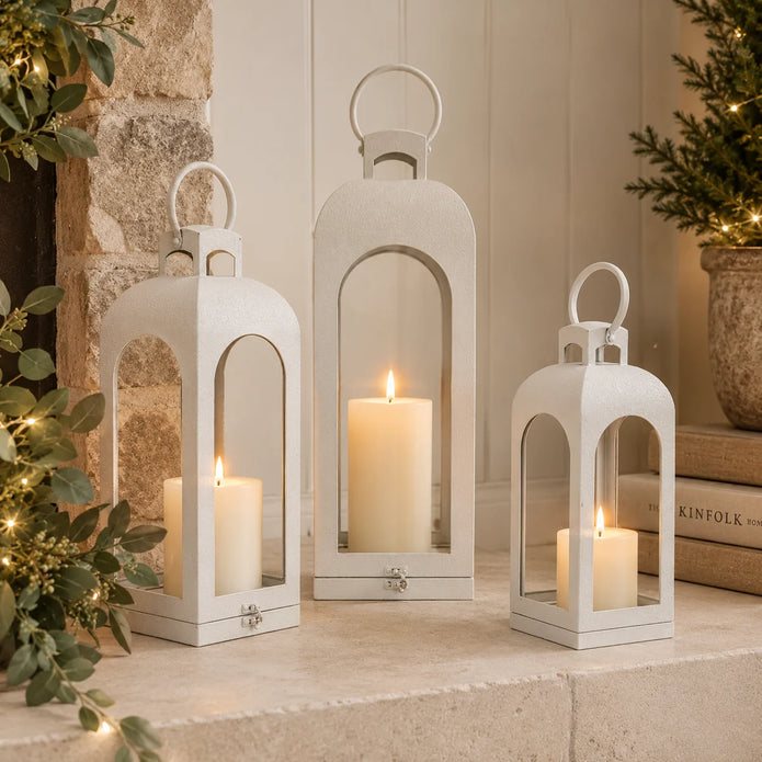 Three sizes of white open-sided metal lanterns with LED candles styled together on stone hearth
