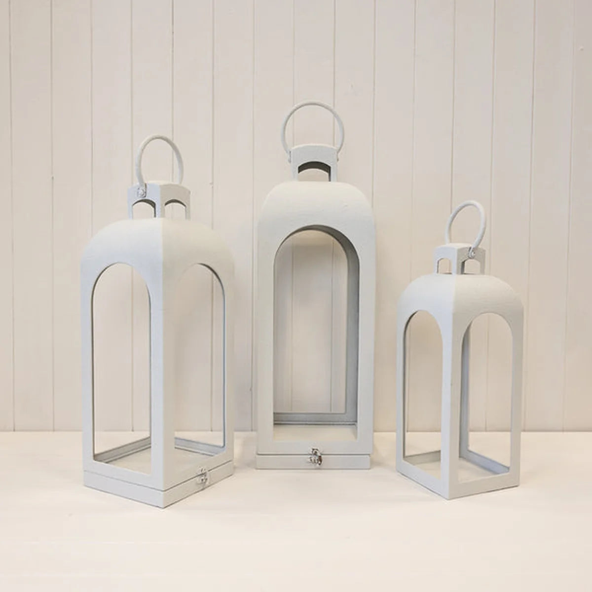 White metal open faced lanterns in three sizes on white background without candles