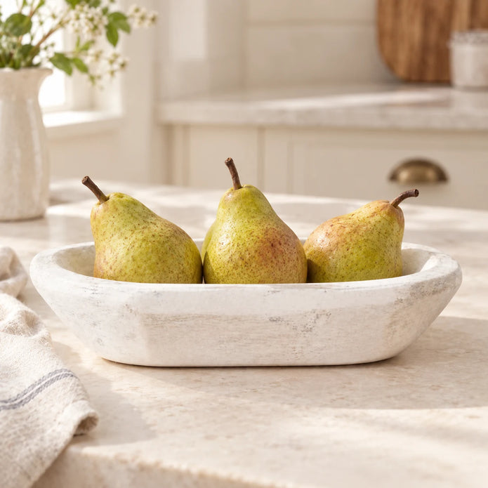 White mini dough bowl holding three pears on a cream kitchen worktop, with folded linen beside it.