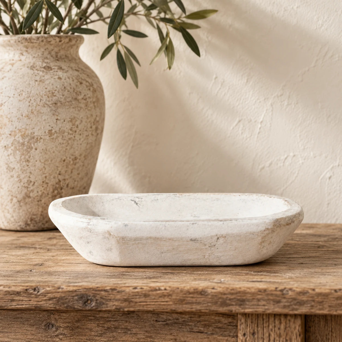 White mini dough bowl styled empty on an oak console beside a tall stone-coloured vase and olive foliage.