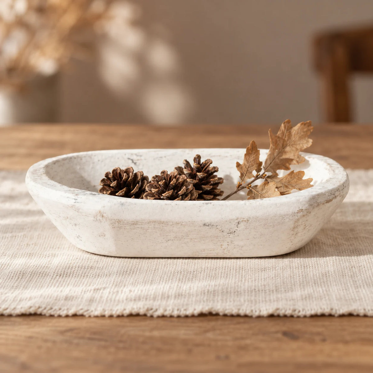 White wooden mini dough bowl styled with pine cones and a dried oak sprig on cream linen.
