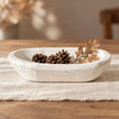 White wooden mini dough bowl styled with pine cones and a dried oak sprig on cream linen.