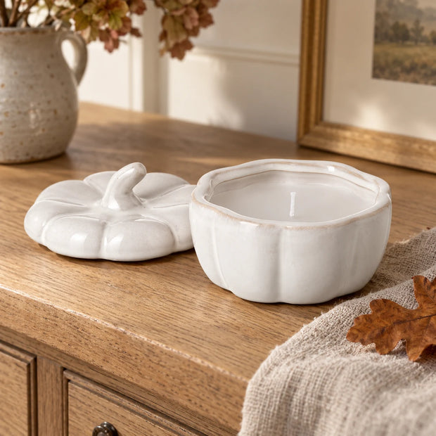 Unlit white porcelain pumpkin candle with lid beside it on an oak console.