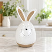 White ceramic rabbit on a pale kitchen counter with green foliage behind.