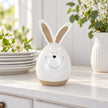 White ceramic rabbit beside stacked white plates on a kitchen dresser.