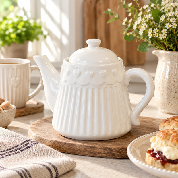 White ribbed ceramic teapot with raised heart pattern styled on a wooden board in a bright country kitchen