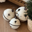 White Round Hanging Metal Bells, white metal bells grouped on a wooden shelf beside greenery