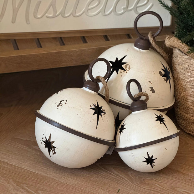 White Round Hanging Metal Bells, three white metal bells with dark star cutouts on a shelf