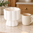 White scalloped pedestal wax melt and oil burner by Something Different Wholesale beside a kitchen scale