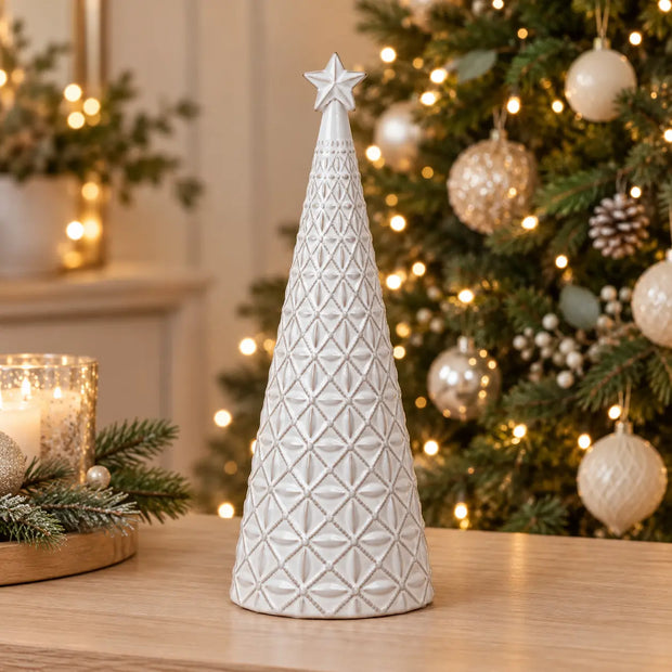 Medium white star glazed ceramic Christmas tree by Satchville, decorated for holiday celebration, displayed on a console table.