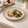White stoneware dinner plate holding salad and bread on a light kitchen island
