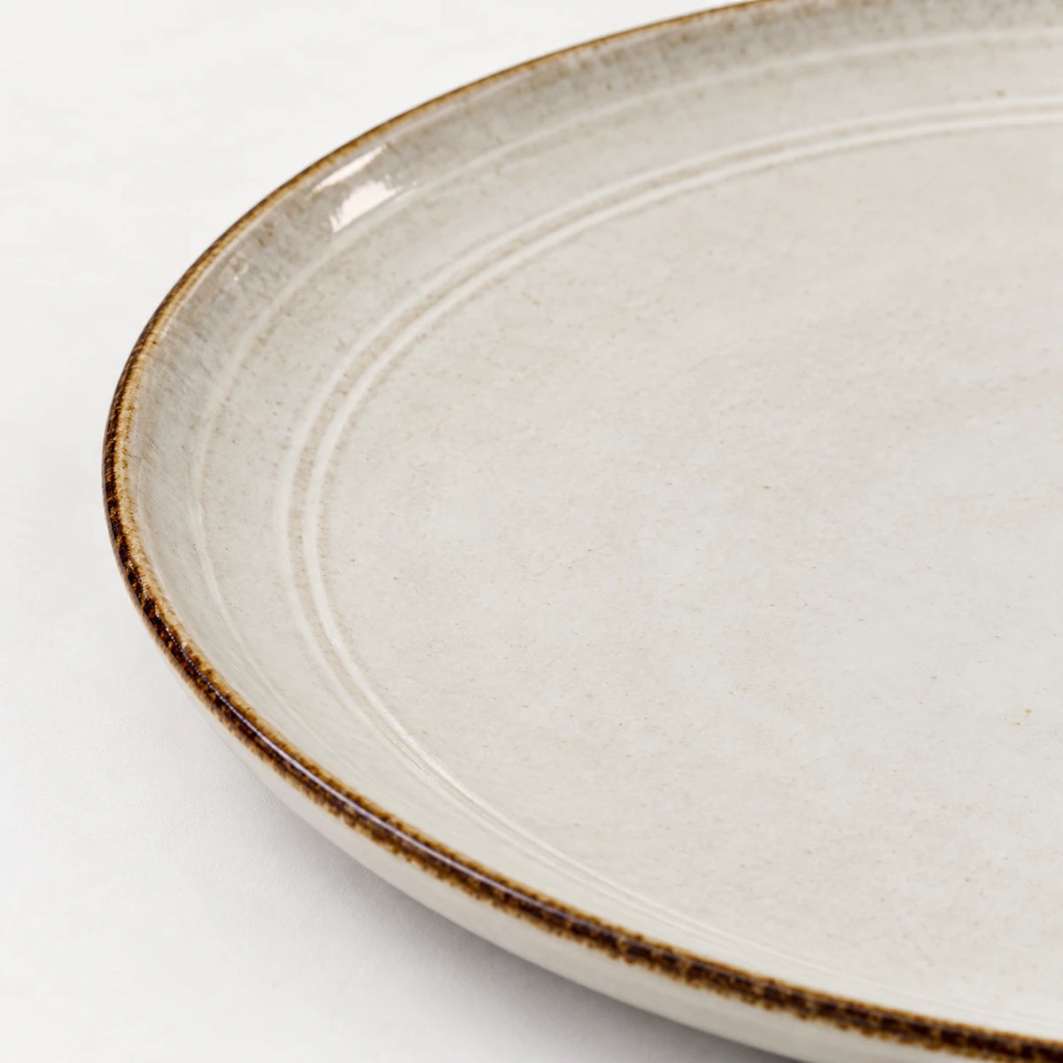 Close-up of the brown rim and shallow concentric rings on a white stoneware dinner plate