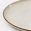 Close-up of the brown rim and shallow concentric rings on a white stoneware dinner plate