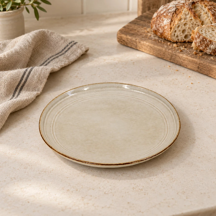Empty white stoneware side plate on a light kitchen worktop beside bread and linen