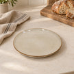 Empty white stoneware side plate on a light kitchen worktop beside bread and linen