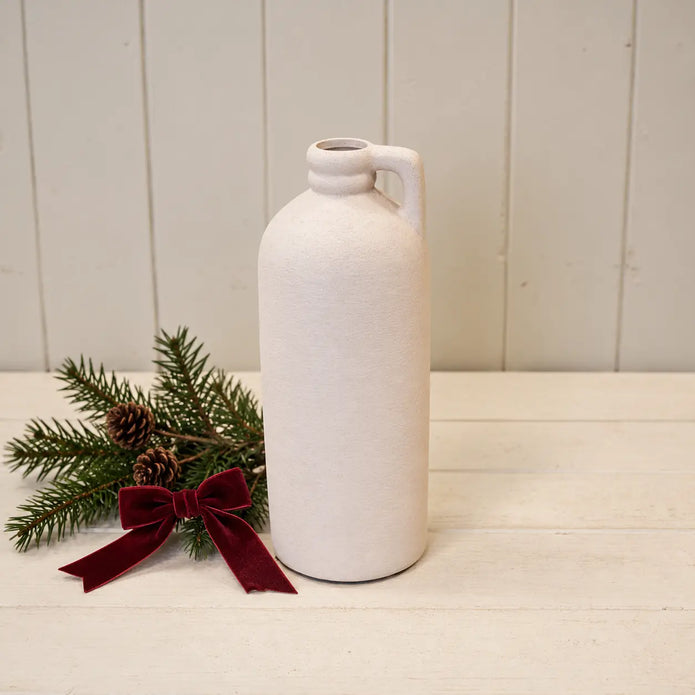 White tall bottle vase beside evergreen foliage and burgundy bow