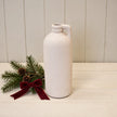 White tall bottle vase beside evergreen foliage and burgundy bow