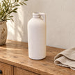 White textured bottle vase displayed empty on a rustic oak sideboard