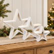 Three graduated white wooden stars on a sideboard with neutral Christmas decorations