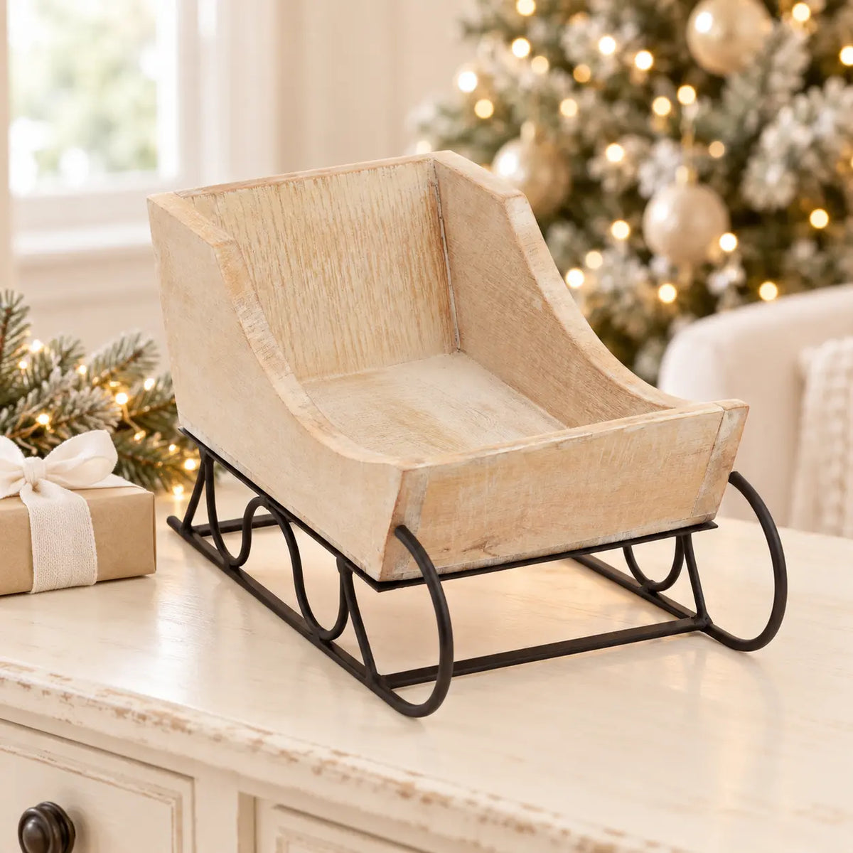 Empty whitewashed wooden sleigh on a light table beside a Christmas tree