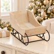 Empty whitewashed wooden sleigh on a light table beside a Christmas tree