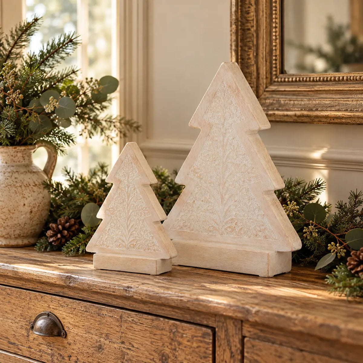 Two sizes of carved whitewashed wooden Christmas trees on an oak console