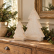 Two sizes of carved whitewashed wooden Christmas trees on an oak console