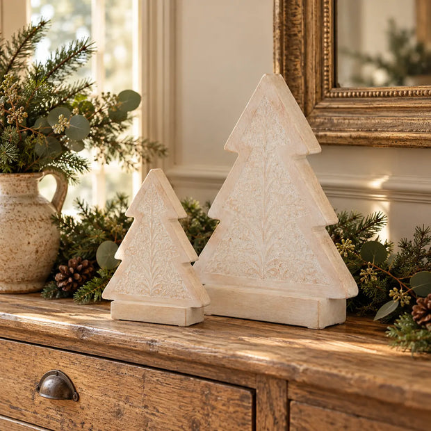Two sizes of carved whitewashed wooden Christmas trees on an oak console