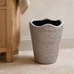 Wickham Rattan Round Lined Waste Paper Bin, pale woven waste bin with dark lining beside a wooden cabinet