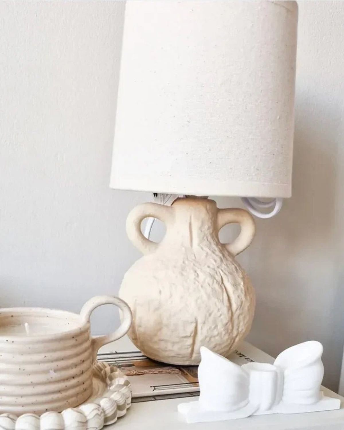 Small cream ceramic table lamp with a ceramic handle and linen shade, perfect for cozy lighting in living spaces.