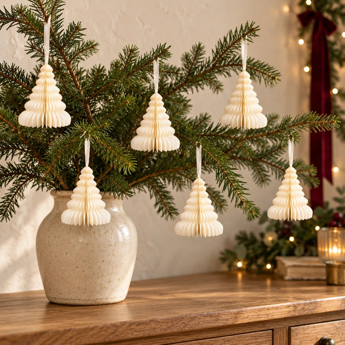 Six winter white paper tree decorations hanging from fir branches above an oak sideboard.