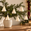 Six winter white paper tree decorations hanging from fir branches above an oak sideboard.