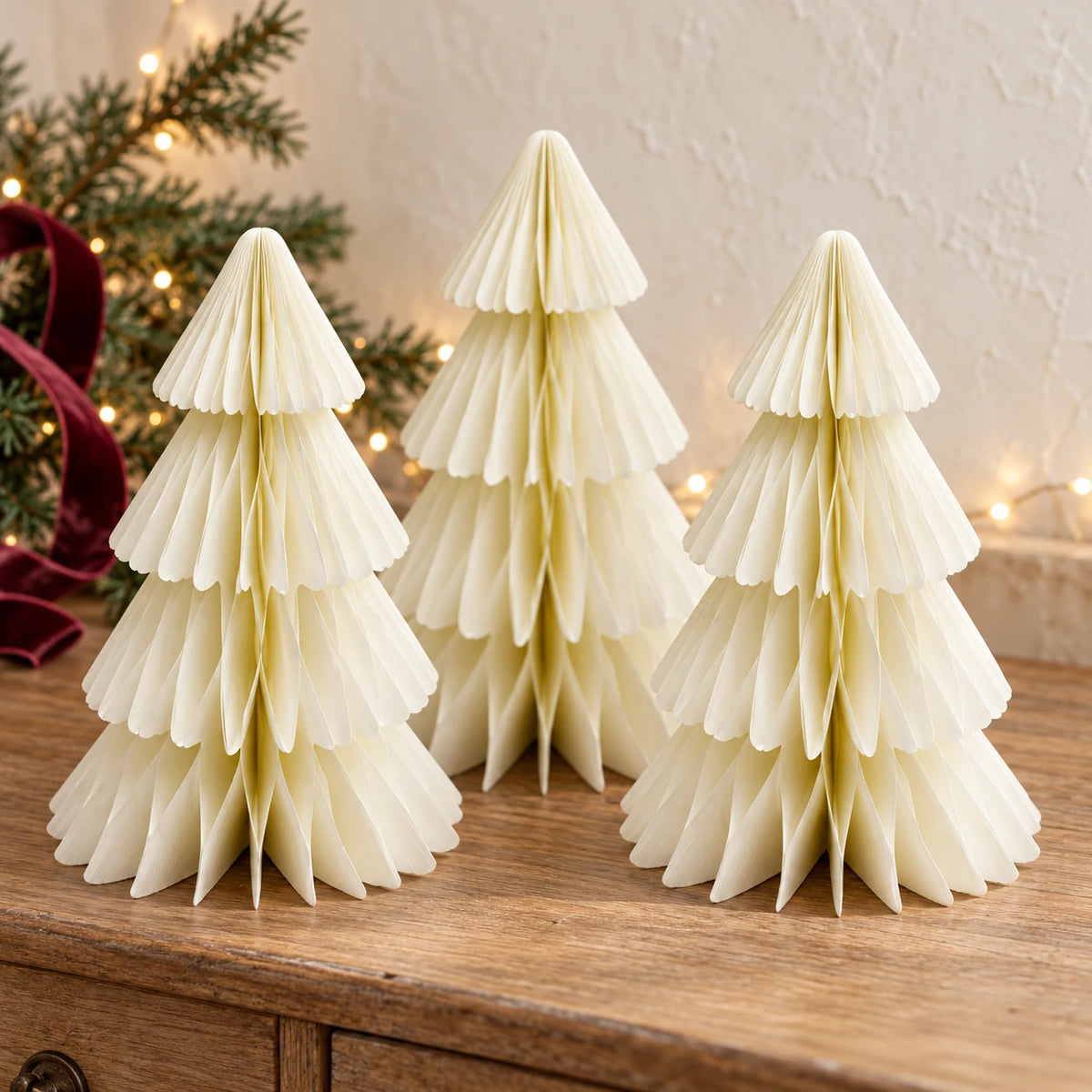 Set of three winter white paper Christmas trees styled on an oak console with fir and burgundy ribbon.