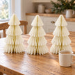 Set of three winter white paper Christmas trees on an oak kitchen table beside a mug of tea.