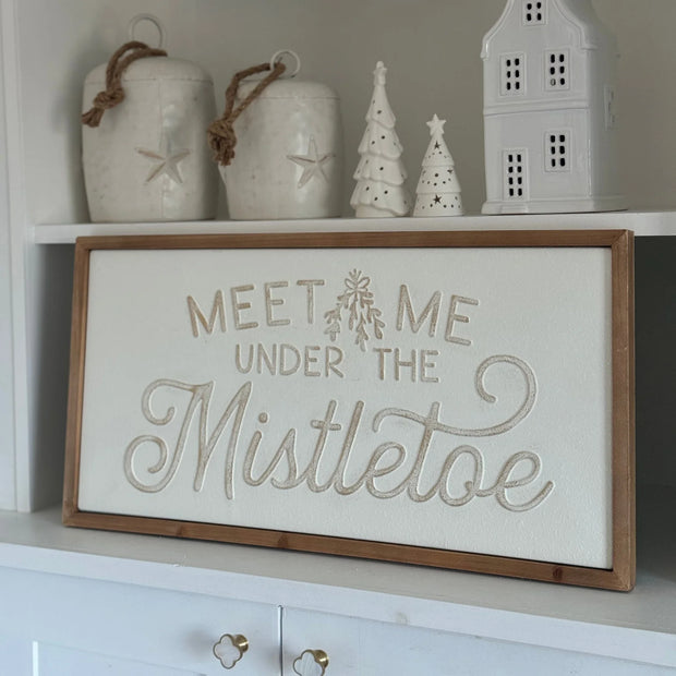 White Meet Me Under the Mistletoe sign below ceramic house ornaments