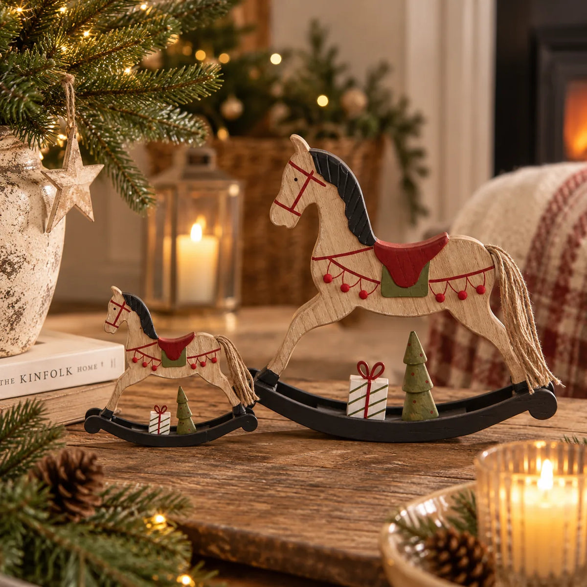 Small and large rustic wooden rocking horse decorations with red saddles and miniature trees in a warm Christmas setting