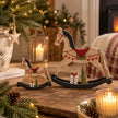 Small and large rustic wooden rocking horse decorations with red saddles and miniature trees in a warm Christmas setting